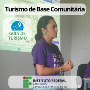 A imagem mostra a professora Adriana da Igreja, que está vestindo uma camiseta roxa com os dizeres "Educação Pública & Federal & Gratuita" e uma calça jeans, está à frente da sala, apresentando um slide projetado na parede. Ela tem cabelos presos e gesticula com as mãos fechadas. Ao fundo há um slide projetado com uma imagem que não é possível distinguir.
Na parte superior da imagem, há um banner com fundo claro e o texto "Turismo de Base Comunitária" em preto. No lado esquerdo, há um ícone azul com um mapa e a frase "Técnico Integrado em GUIA DE TURISMO" em verde. Na parte inferior, o logotipo do Instituto Federal Catarinense Campus São Francisco do Sul.
