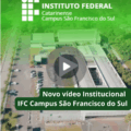 A imagem mostra um enquadramento aéreo do IFC Campus São Francisco do Sul, visto de cima. É possível observar os prédios principais, áreas externas, vagas de estacionamento e a vegetação ao redor do campus. Sobre a imagem há um filtro verde translúcido na parte superior. No canto superior esquerdo está o logotipo do Instituto Federal Catarinense, composto por um conjunto de quadrados brancos formando o símbolo do IF, seguido do texto: “INSTITUTO FEDERAL Catarinense Campus São Francisco do Sul”. No centro da imagem aparece um ícone de “play”, indicando que se trata de uma prévia de vídeo. Na parte inferior, sobreposta à cena, há uma faixa verde escura com o texto em branco: “Novo vídeo Institucional IFC Campus São Francisco do Sul”.