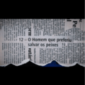 A imagem mostra um recorte de jornal rasgado de forma irregular, revelando ao centro o título “12 – O Homem que preferiu salvar os peixes” em destaque. O recorte está posicionado sobre um fundo azul escuro que aparece pela abertura criada pelo rasgo na parte inferior. Ao redor do título, é possível ver trechos de textos jornalísticos desfocados e dispostos vertical e horizontalmente, reforçando o aspecto de colagem. A área superior e inferior da imagem está preenchida por faixas pretas, criando contraste e direcionando a atenção para o recorte central onde aparece o título da obra.