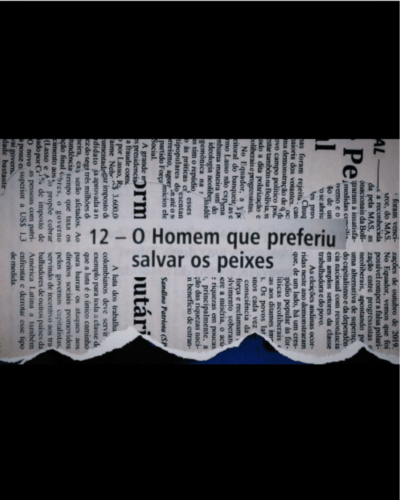 A imagem mostra um recorte de jornal rasgado de forma irregular, revelando ao centro o título “12 – O Homem que preferiu salvar os peixes” em destaque. O recorte está posicionado sobre um fundo azul escuro que aparece pela abertura criada pelo rasgo na parte inferior. Ao redor do título, é possível ver trechos de textos jornalísticos desfocados e dispostos vertical e horizontalmente, reforçando o aspecto de colagem. A área superior e inferior da imagem está preenchida por faixas pretas, criando contraste e direcionando a atenção para o recorte central onde aparece o título da obra.